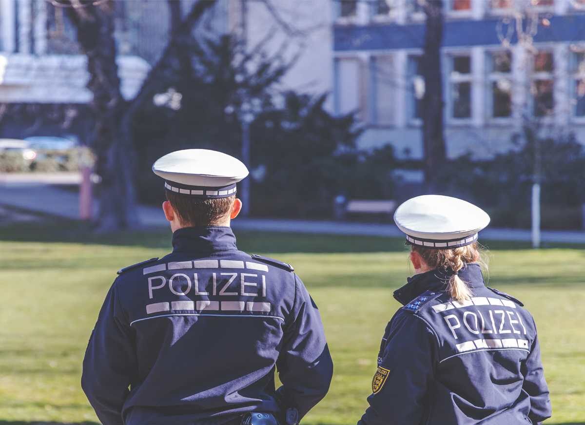 Zwei Polizisten von hinten, die vor einer Wiese stehen. Blauer Textbanner mit Polizeistern: Sicherheitstag 2023.